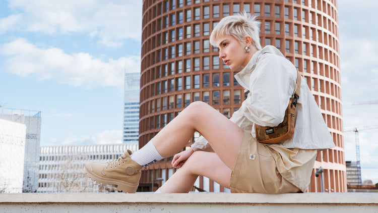 Person sitting on a ledge with a cityscape background wearing Palladium Pallabase Twill boots