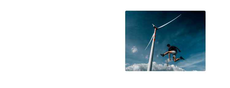 A person leaps near a tall wind turbine under a blue sky, wearing Palladium boots, showcasing freedom.