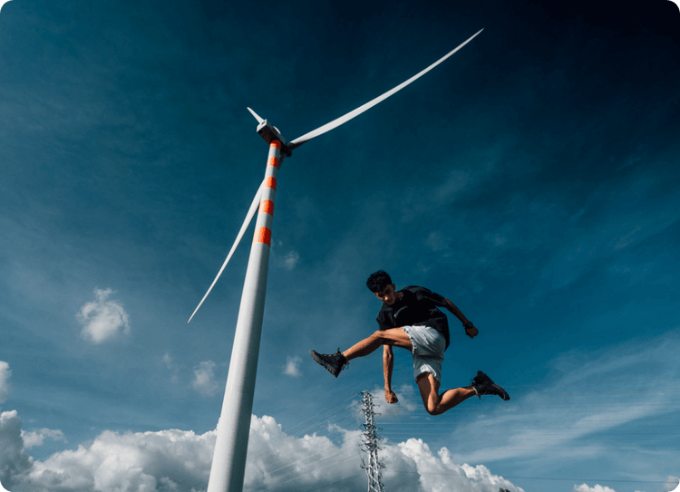 A person leaps near a tall wind turbine under a blue sky, wearing Palladium boots, showcasing freedom.