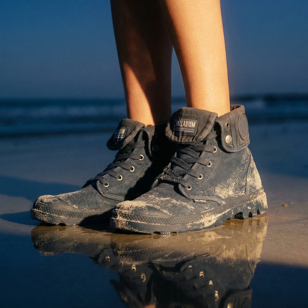 Black boots on a beach with ocean reflection