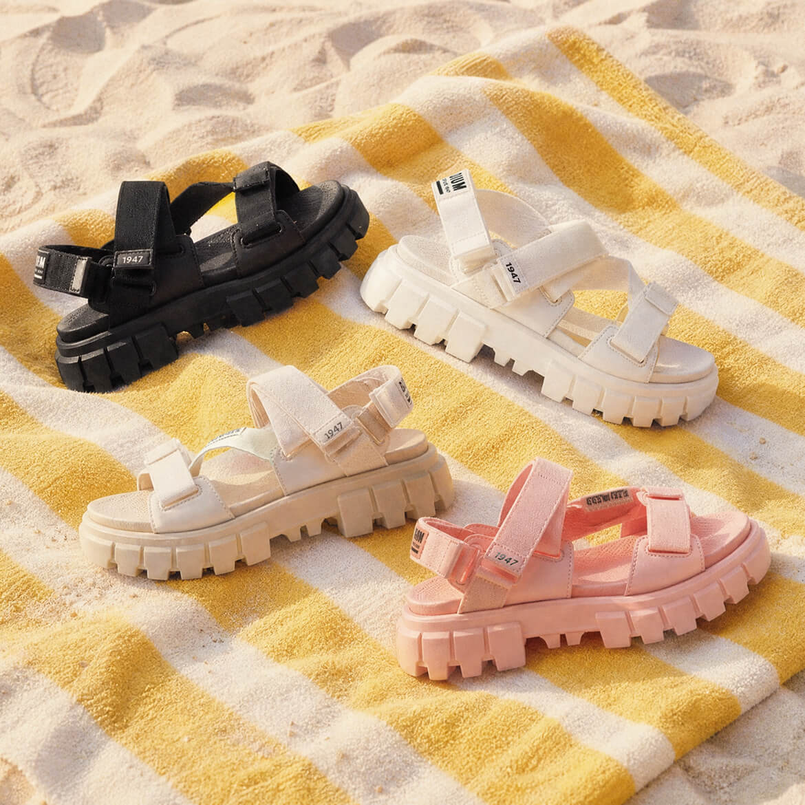 Four pairs of sandals in black, white, and pink on a yellow and white striped towel.