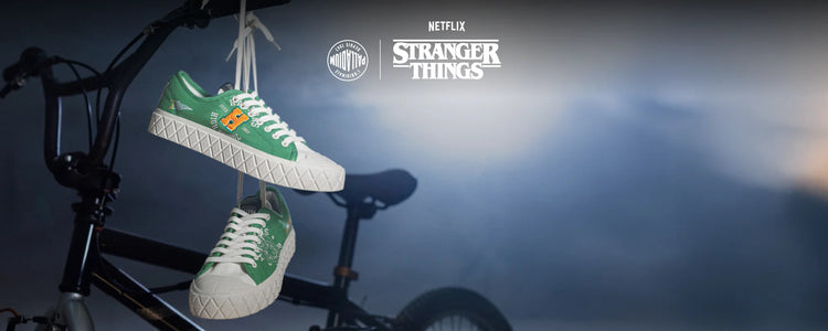 Green and white sneakers hanging from a bike with 'Stranger Things' branding in the background.