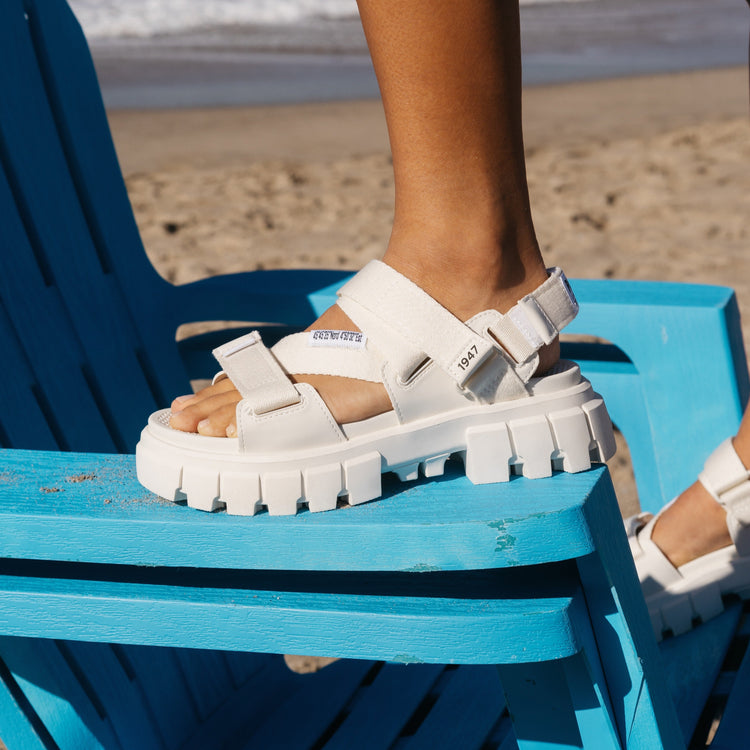 Photo of someone standing on a chair on the beach wearing the Revolt Sandal Mono